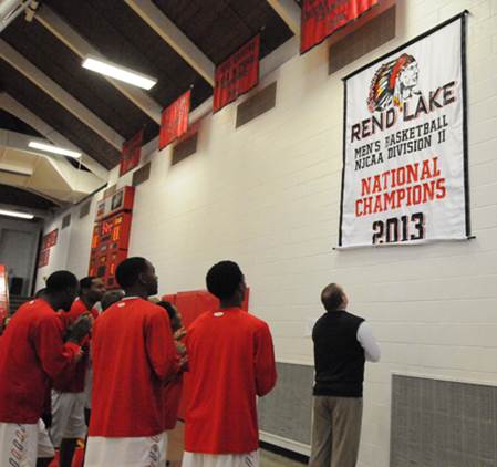 Rend Lake College Warriors Head Coach Randy House, RIGHT, unveils the 2013 National Championship banner Sunday afternoon before the Warriors game against Illinois Central. The new feature to Waugh Gymnasium was not the only change - the team also donned new white jerseys. (ReAnne Palmer / RLC Public Information)